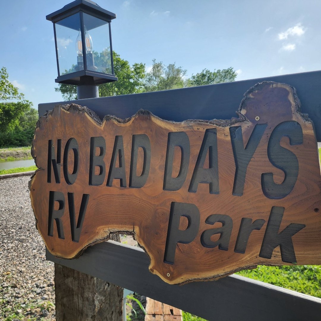 Hand-carved wooden No Bad Days RV Park entrance sign under a Texas sky